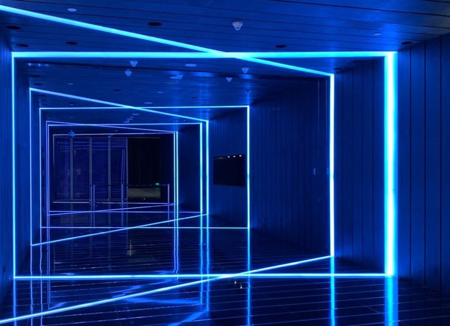 Blaue beleuchteter Gang mit in Decke, Wände und Böden integrierte Linienleuchten und reflektierendem Boden.
